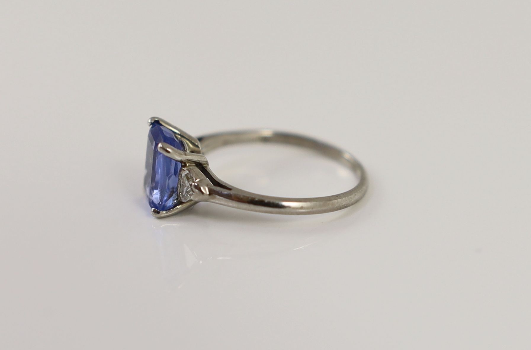 A platinum and palladium set single stone cushion cut sapphire ring, with triangular cut diamond set shoulders